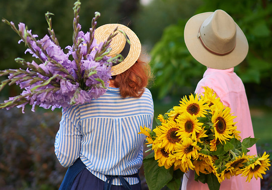 With their backs turned to the camera, a pair of sisters hoist lovely bouquets of purple and yellow flowers over their shoulders